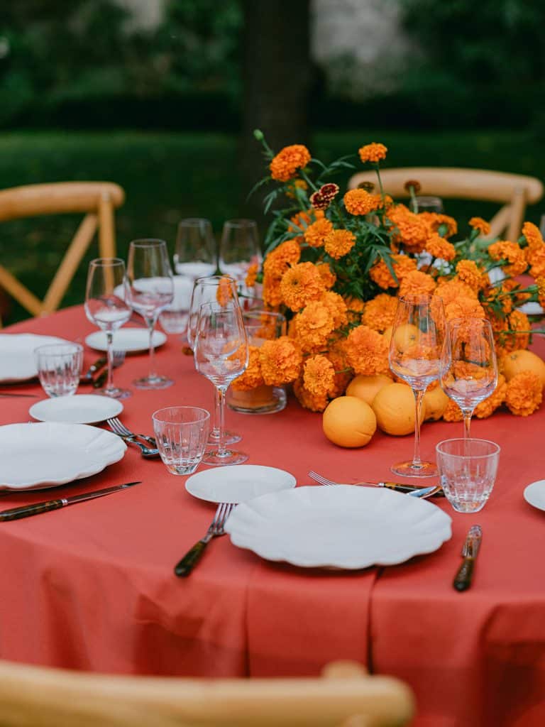 Dîner de bienvenue dans le potager du Domaine de Primard – table monochrome orange avec œillets d’Inde, bougies et oranges fraîches.