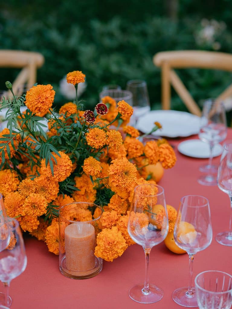 Dîner de bienvenue dans le potager du Domaine de Primard – table monochrome orange avec œillets d’Inde, bougies et oranges fraîches.